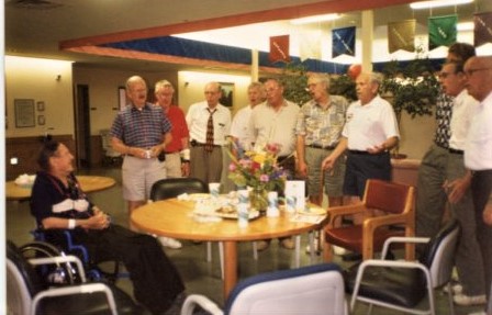 Group of 10 men singing to a person in a nursing home.
