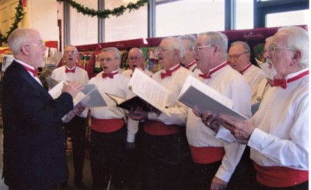 Men in white shirts, red cummerbunds, and red bow ties singing.